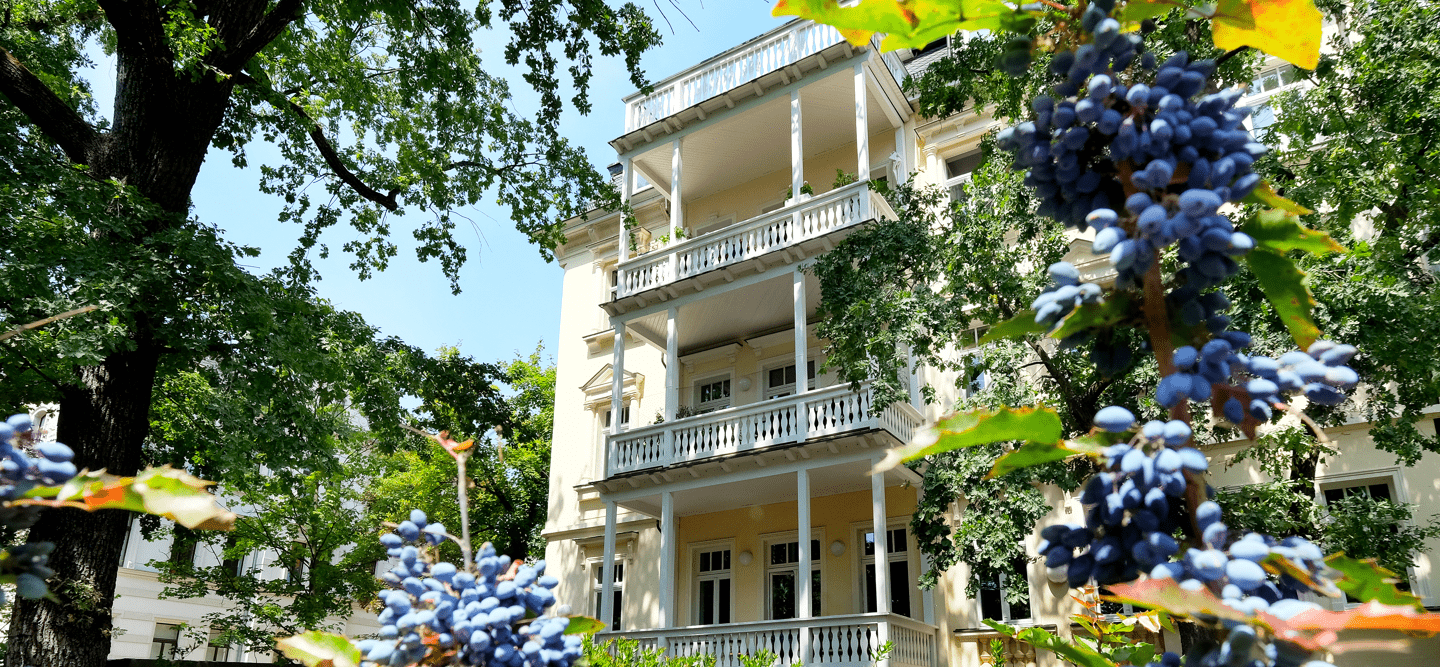 Ein Foto einer sanierten Hauswand mit großen Balkonen im Gründerzeitstil. Das Gebäude ist umgeben von reichlich Natur.