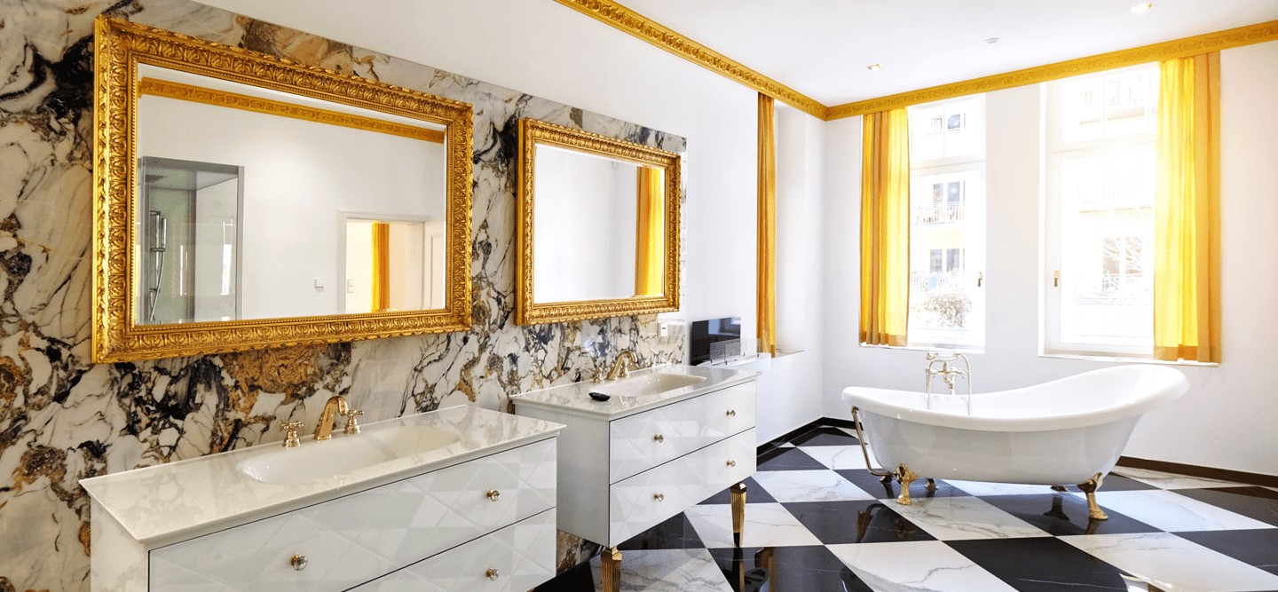 Foto eines Luxusbades mit freistehender Badewanne, Mamor-Fliesen, Goldspiegeln, edlen Waschtischen und vergoldetem Stuck.