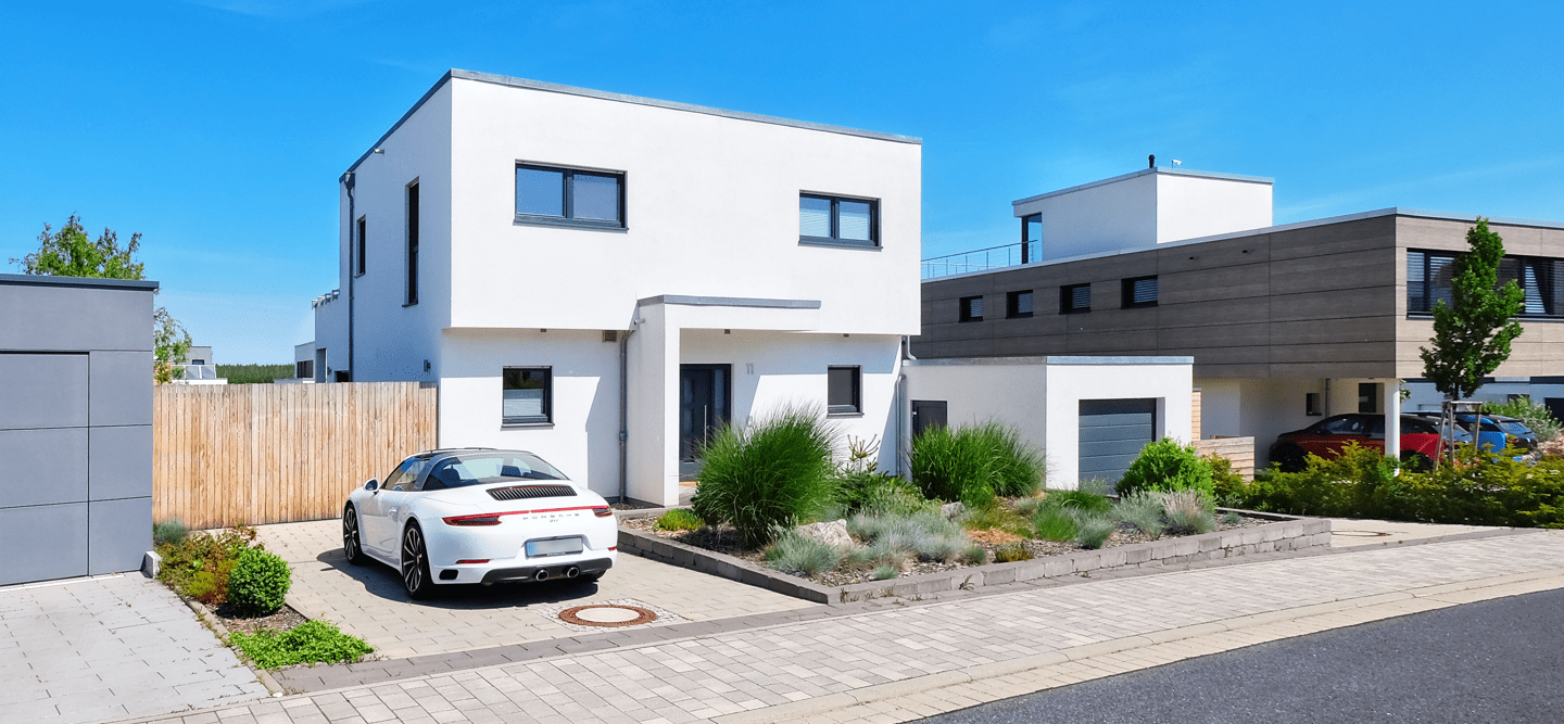 Foto eines modernen Einfamilienhauses mit 2 Etagen und einer Garage. Davor steht ein Porsche.