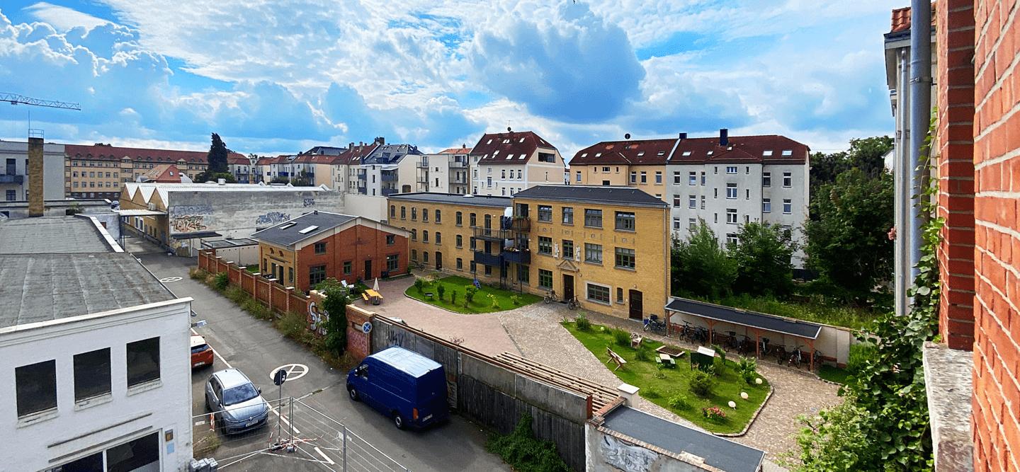 Luftbildaufnahme einer kleinen Straße mit alten Industribauten, Neubau und sanierten Immobilien. Der Himmel ist blau und bewölkt. Hier entsteht das Wohncarré Plagwitz.